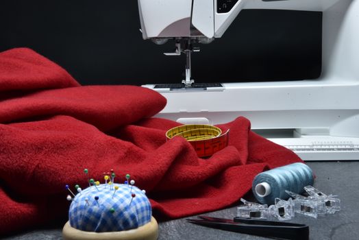 Trousse d'écolier sur mesure avec tissu rouge, épingles, bobines de fil et machine à coudre en arrière-plan.
