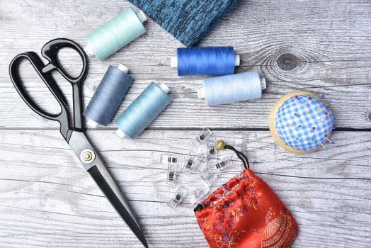 Ciseaux, bobines de fil bleu et rouge, épingles et un petit sac en tissu sur une table en bois.